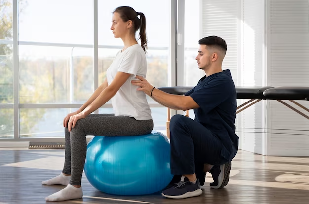 Therapist correcting the posture of a woman sitting on a gym ball.