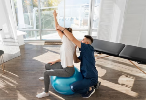 Therapist stretching woman's body while sitting on an exercise ball.