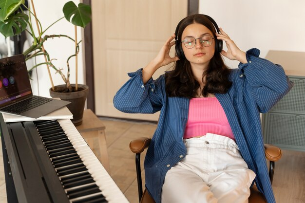 Female with headphones on, listening beside a keyboard.